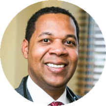 Professional headshot of a smiling man in a dark suit and red tie.